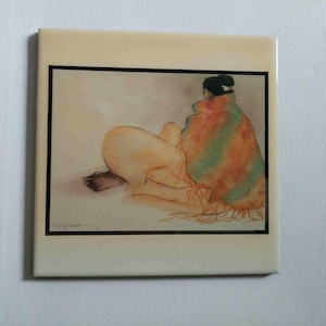 May include: A ceramic tile with an artistic illustration of a person wrapped in a colourful blanket. The artwork is framed with a black border and set against a cream-coloured background. The person is depicted in a relaxed pose.