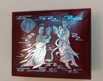 May include: A red wooden box with a mother of pearl inlay design of two figures in flowing robes with a full moon in the background.
