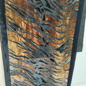 May include: A rectangular panel featuring a textured, golden-brown wood grain surface overlaid with a glossy black, abstract, organic pattern of flowing, irregular lines that resemble tiger stripes, framed by a solid black border on the sides.