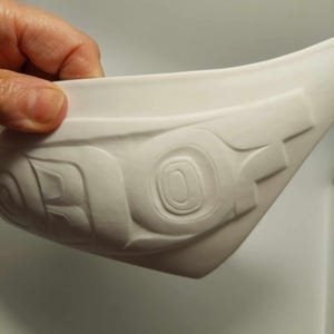 Könnte beinhalten: Weiße Keramikschale mit einem geschnitzten Design. Das Design zeigt eine Reihe konzentrischer Kreise und Linien, die ein geometrisches Muster bilden.