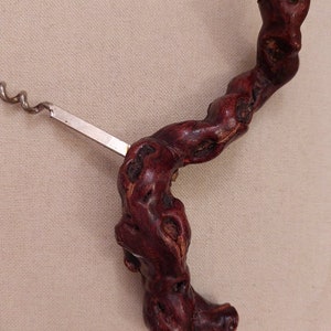 May include: A wooden corkscrew with a dark red finish and a silver metal worm. The handle is shaped like a twisted branch.