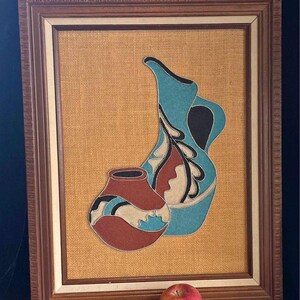May include: A framed artwork featuring two stylized pottery pieces in shades of blue, brown, and white, set against a burlap background.
