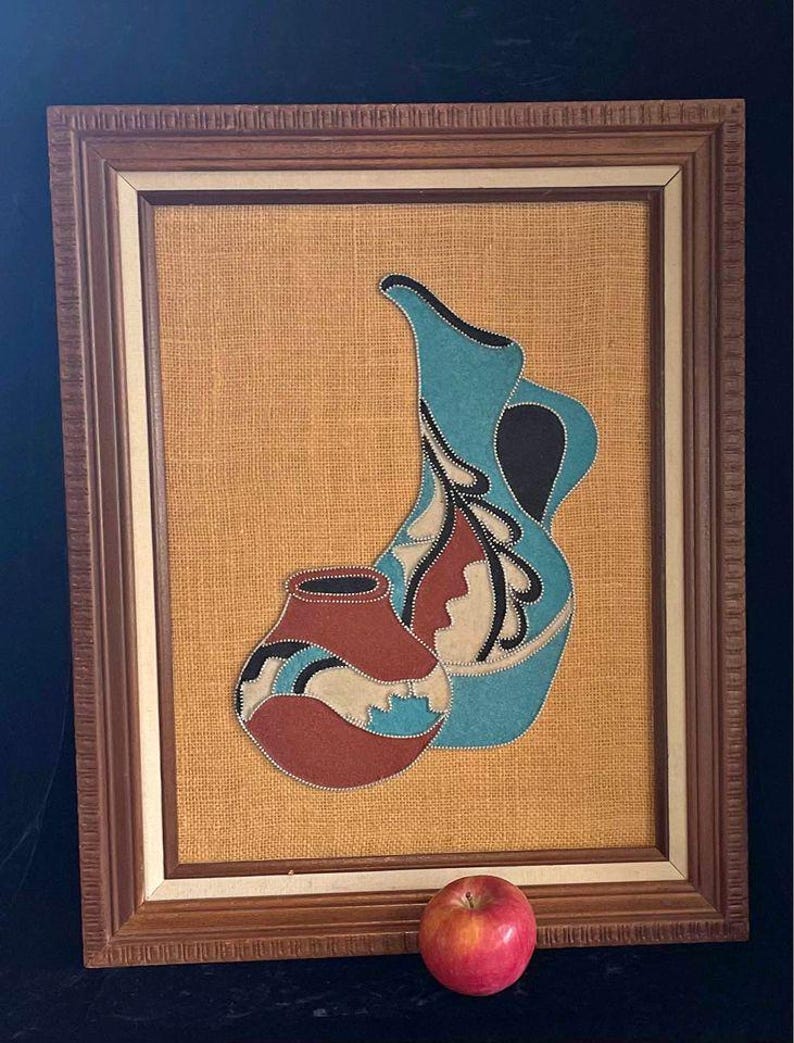 May include: A framed artwork featuring two stylized pottery pieces in shades of blue, brown, and white, set against a burlap background.
