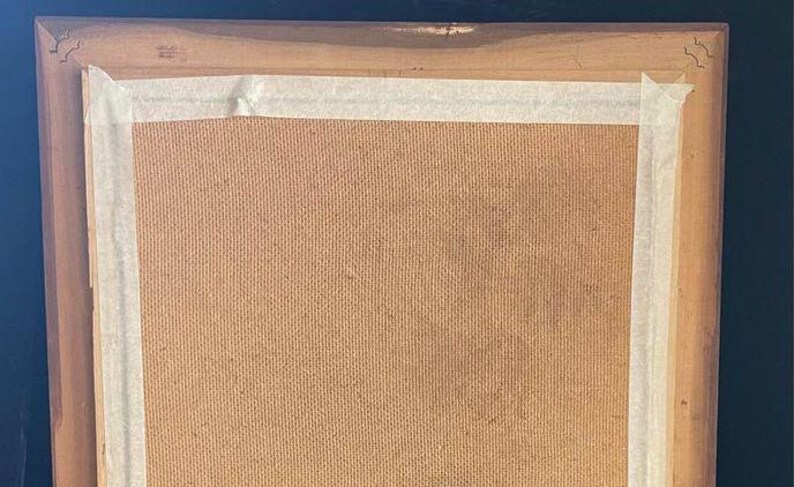 May include: A wooden picture frame with a brown cardboard backing. The frame has a light brown finish and is covered with white tape.