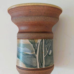 Peut inclure: Un vase en céramique fait à la main avec un dessus évasé et une base cylindrique. Le vase présente un paysage avec des arbres verts et bleus. Le vase mesure environ 15 cm de haut.