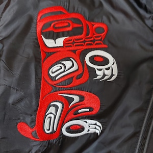 May include: Black jacket with a red and white embroidered design of a stylized bear. The bear is in a traditional Native American style.
