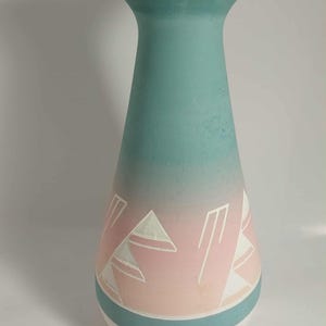 May include: A tall, decorative vase with a turquoise top that fades into a pink and white geometric design. The vase has a white base with a turquoise band. The vase is likely ceramic and suitable for home decor.