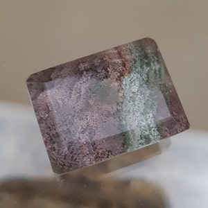 Può includere: Una pietra preziosa rettangolare sfaccettata con un motivo di colore verde, rosa e bianco. La pietra preziosa ha un aspetto nuvoloso e traslucido.