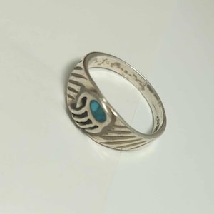 May include: A silver ring featuring a bear claw design with a small, oval-shaped turquoise inlay. The band is decorated with etched diagonal lines that extend from the claw motif, creating a textured appearance around the metal surface.