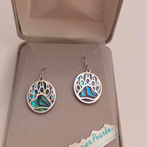 May include: A pair of silver bear paw earrings with a blue and green abalone shell inlay. The earrings are in a small box with a "Glacier Pearle" label. Hypoallergenic posts.