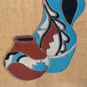 May include: A framed artwork featuring two stylized pottery pieces, one blue and one red, with white and black accents. The artwork is made of fabric and beads, and is set against a burlap background.