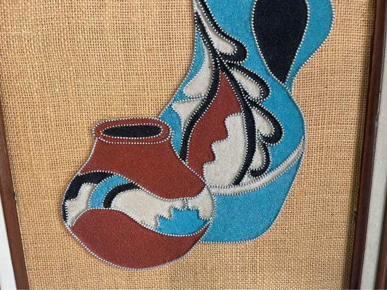 May include: A framed artwork featuring two stylized pottery pieces, one blue and one red, with white and black accents. The artwork is made of fabric and beads, and is set against a burlap background.