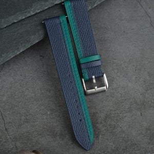 Pode incluir: Pulseira de relógio azul e verde com um padrão texturizado. A pulseira tem uma faixa verde no centro e uma fivela prateada. O texto "Handmade by Vitalis Leather Goods" é visível.