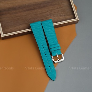 Puede incluir: Correas de reloj de cuero turquesa con hebilla plateada. Las correas se muestran sobre una superficie marrón y naranja. El texto "Vitalis Leather Goods" es visible.