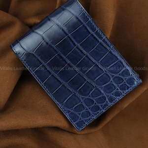 Könnte beinhalten: Ein marineblaues Lederportemonnaie mit Krokodilhautmuster. Das Portemonnaie ist rechteckig und scheint gefaltet zu sein. Die Worte "Handmade by Vitalis Leather Goods" sind im Bild zu sehen.