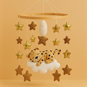 Op de afbeelding: Baby mobile met een slapende luipaard op een wolk, omringd door gouden en bruine sterren. De mobiel heeft een houten ring en een wit eivormig element. Een charmante decoratie voor de kinderkamer.