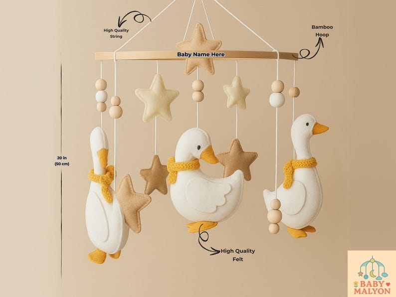 Op de afbeelding: Een baby mobile met drie witte vilten ganzen met gele accenten en stervormige ornamenten. De mobiel is opgehangen aan een houten frame en meet 50 cm in lengte. Inclusief hoogwaardig touw en vilt.