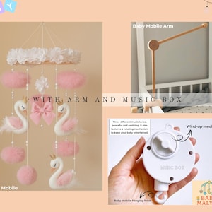 Op de afbeelding: Een baby mobile met een zwanenthema, met witte zwanen met roze accenten, roze pompons en een witte bloemen top. De mobiel bevat een muziekdoos en arm voor eenvoudige installatie. De tekst "WITH ARM AND MUSIC BOX" is zichtbaar.
