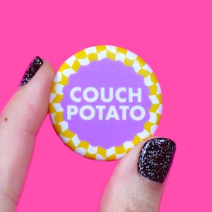 Könnte beinhalten: Ein lila und gelber Knopf mit dem Text "COUCH POTATO" darauf.