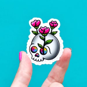 May include: A white skull sticker with a rainbow eye and pink flowers growing out of the top of the skull.