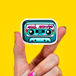 May include: A blue and white cassette tape sticker with a sad face and the text "sad songs".