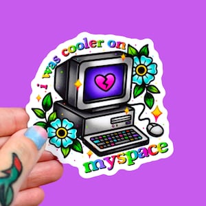 May include: A sticker featuring a retro computer with a broken heart on the screen, surrounded by flowers and stars. The text reads "I was cooler on myspace" in a colorful, playful font. The sticker is held against a purple background.