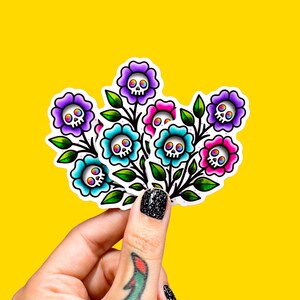 May include: A sticker featuring a bouquet of flowers with skull faces. The flowers are in shades of purple, pink, and turquoise, with green leaves and black stems. The background is a bright yellow.
