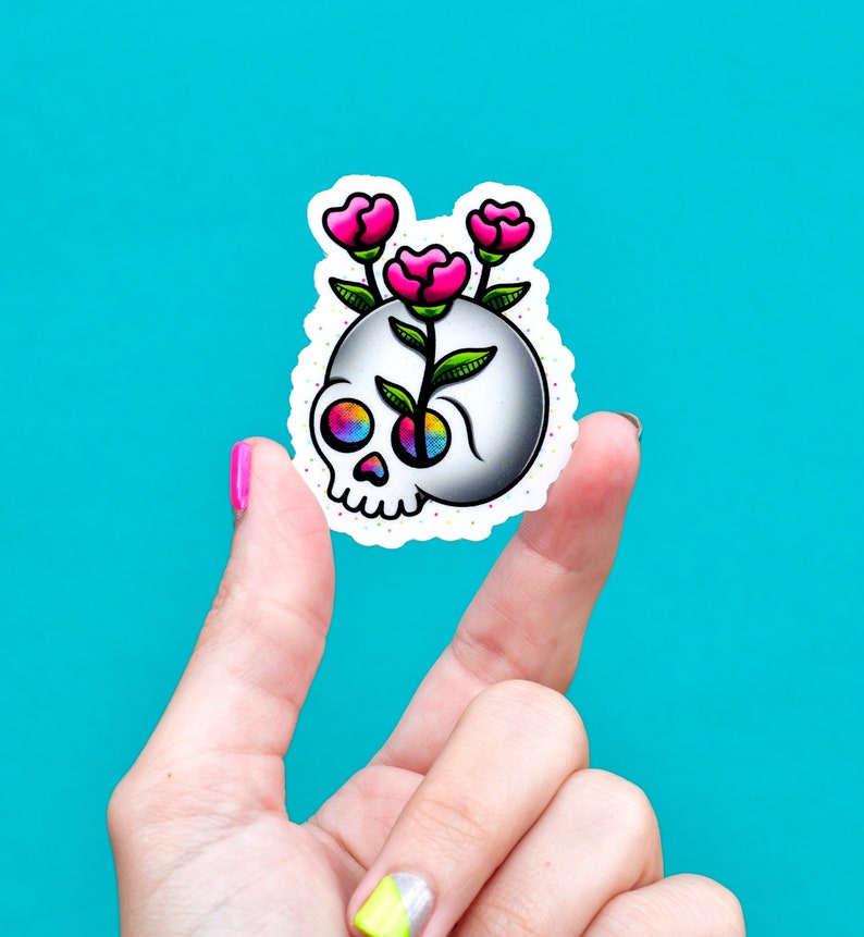 May include: A white skull sticker with a rainbow eye and pink flowers growing out of the top of the skull.