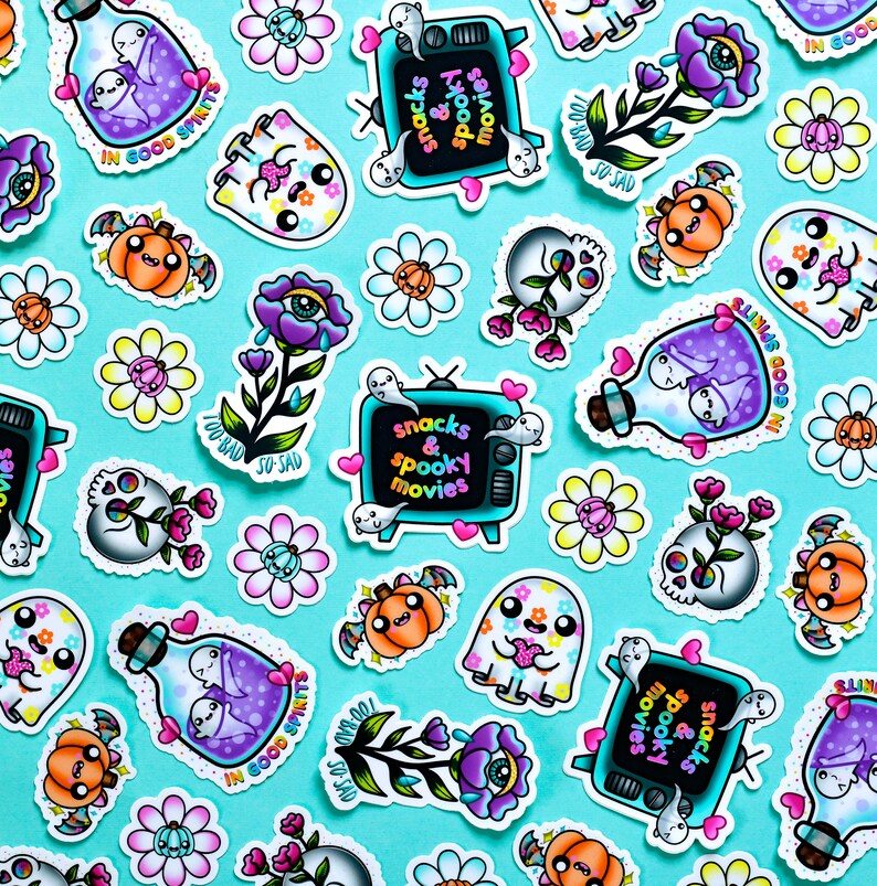 May include: A collection of colorful stickers featuring spooky and cute Halloween themes. The stickers include ghosts, pumpkins, flowers, skulls, and a television with the text "snacks & spooky movies".