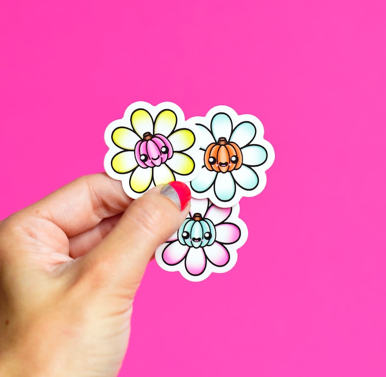 May include: Three colorful flower stickers with a pumpkin face in the center. The flowers are yellow, blue, and pink.