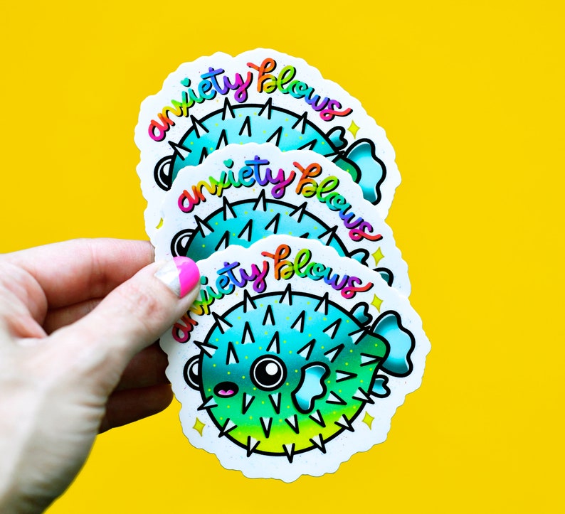 May include: Three colorful stickers with a cartoon pufferfish and the text "anxiety blows" in rainbow letters. The stickers are layered on top of each other.