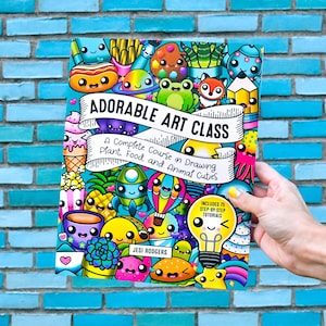 May include: A colorful book titled "Adorable Art Class" featuring cartoon drawings of food, plants, and animals. The cover includes the text "A Complete Course in Drawing Plant, Food, and Animal Cuties" and "Includes 75 Step-by-Step Tutorials".