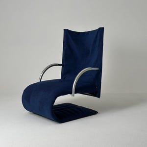 May include: A blue upholstered chair with a curved, metal frame. The chair has a high back and a footrest.