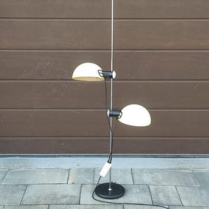 以下が含まれることがあります： 2つのオフホワイトの半円形シェードが付いたヴィンテージフロアランプ。ランプは黒いベースと細いシルバーのポールを備えています。シェードは黒い備品でポールに取り付けられています。白いハンドルがベースの近くにあります。