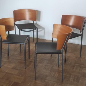 May include: Four chairs with black metal frames and wooden backs. The chairs are arranged in a circle on a wood floor.