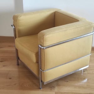 Könnte beinhalten: Ein gelber Sessel mit einem verchromten Gestell. Der Sessel hat eine quadratische Form und ist mit einem weichen, gelben Stoff bezogen.