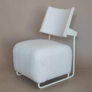 May include: A modern white chair with a square, cushioned seat and a curved backrest. The chair has a white metal frame and is upholstered in a soft, textured white fabric. The design is minimalist and contemporary.