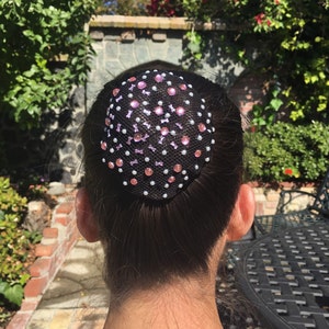 May include: A black hair net with pink and white rhinestones. The hair net is worn on a person's head.
