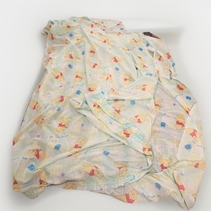 May include: A lightweight fabric sheet featuring a repeating pattern of Winnie the Pooh characters in yellow and red, interspersed with small blue honey pots and the text "gotta bee me" printed in a light blue script across the white background.