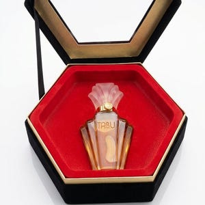 May include: A vintage perfume bottle labeled "TABU" inside a black and gold hexagonal box with a red interior. The perfume bottle is clear with a gold-colored liquid and a decorative top.