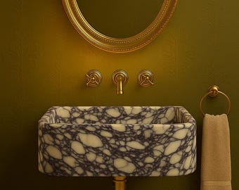 May include: A luxurious bathroom vanity set against a green patterned wall. The set includes a marble sink with a unique veined pattern, gold fixtures, a gold-framed oval mirror, and a matching towel ring with a beige towel.