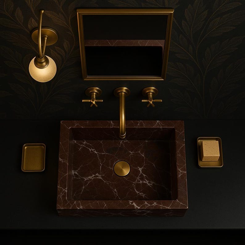 Op de afbeelding: Een bruine marmeren wastafel met een gouden kraan en twee gouden handvatten. De wastafel is geplaatst tegen een zwarte achtergrond met een gouden spiegel erboven.