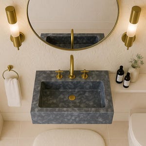May include: A contemporary bathroom suite featuring a grey rectangular sink with gold taps and a circular gold mirror. Two gold wall lights are either side of the mirror. An oval white rug is on the floor. The walls have a floral pattern.