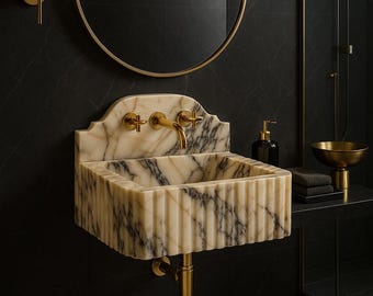 May include: A marble bathroom sink with gold fixtures, set against a black tiled wall. The sink has a fluted design and is paired with a round gold mirror and a wall-mounted light fixture. A small rug is on the floor.