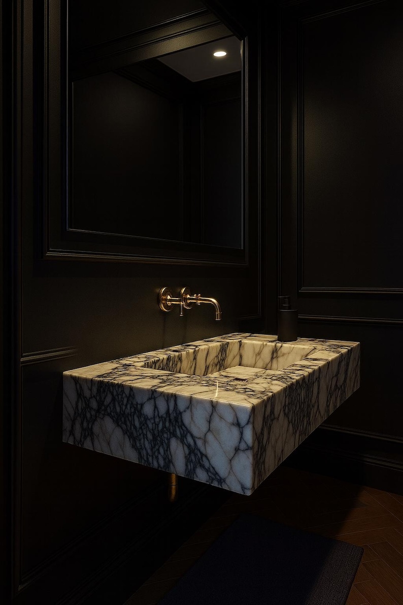 May include: A modern bathroom sink made of marble with dark gray veining. The sink is mounted on a black wall, with a gold faucet and a black soap dispenser. A mirror is above the sink.