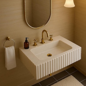 May include: A modern bathroom sink with a gold faucet and fixtures. The white sink has a ribbed design and is mounted on the wall. A gold-framed oval mirror hangs above the sink, and a white towel hangs on a gold towel ring.