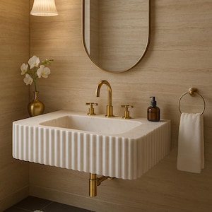 May include: A modern bathroom scene featuring a white marble sink with a fluted design, gold fixtures, and an oval mirror. A small vase with white flowers and a pendant light complete the elegant aesthetic.