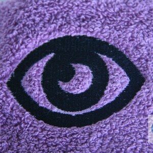 May include: Purple towel with a black embroidered eye design.