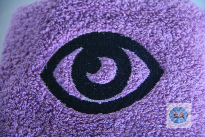 May include: Purple towel with a black embroidered eye design.