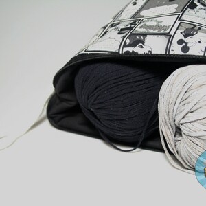 May include: A black and white comic book print zippered bag with a black drawstring. The bag is filled with two balls of yarn, one black and one white.